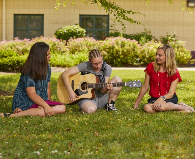 Adolescent female playing guitar for two staff members