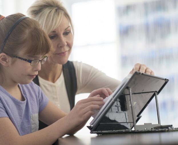 Woman assisting girl with tablet